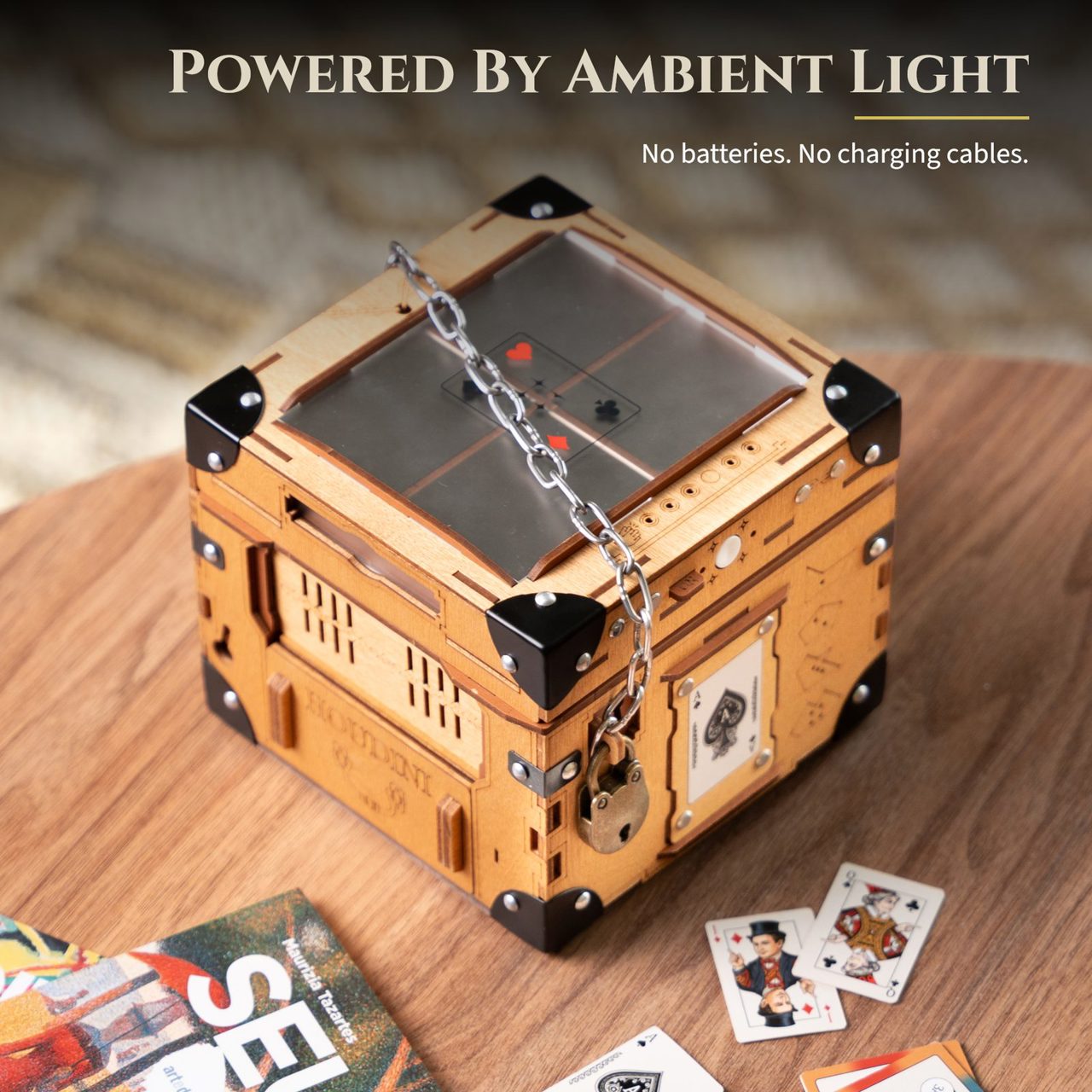 Powered by ambient light, no batteries and no charging cables. The solar panel in the lid seen from above, a playing card visible beneath the glass.